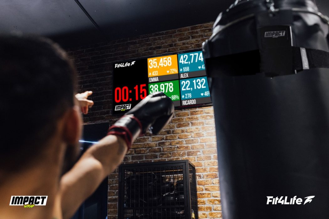 Man wearing boxing gloves during heavy bag workout points at the Impact Wrap leaderboard which shows striking performance score and heart rate and calorie metrics.
